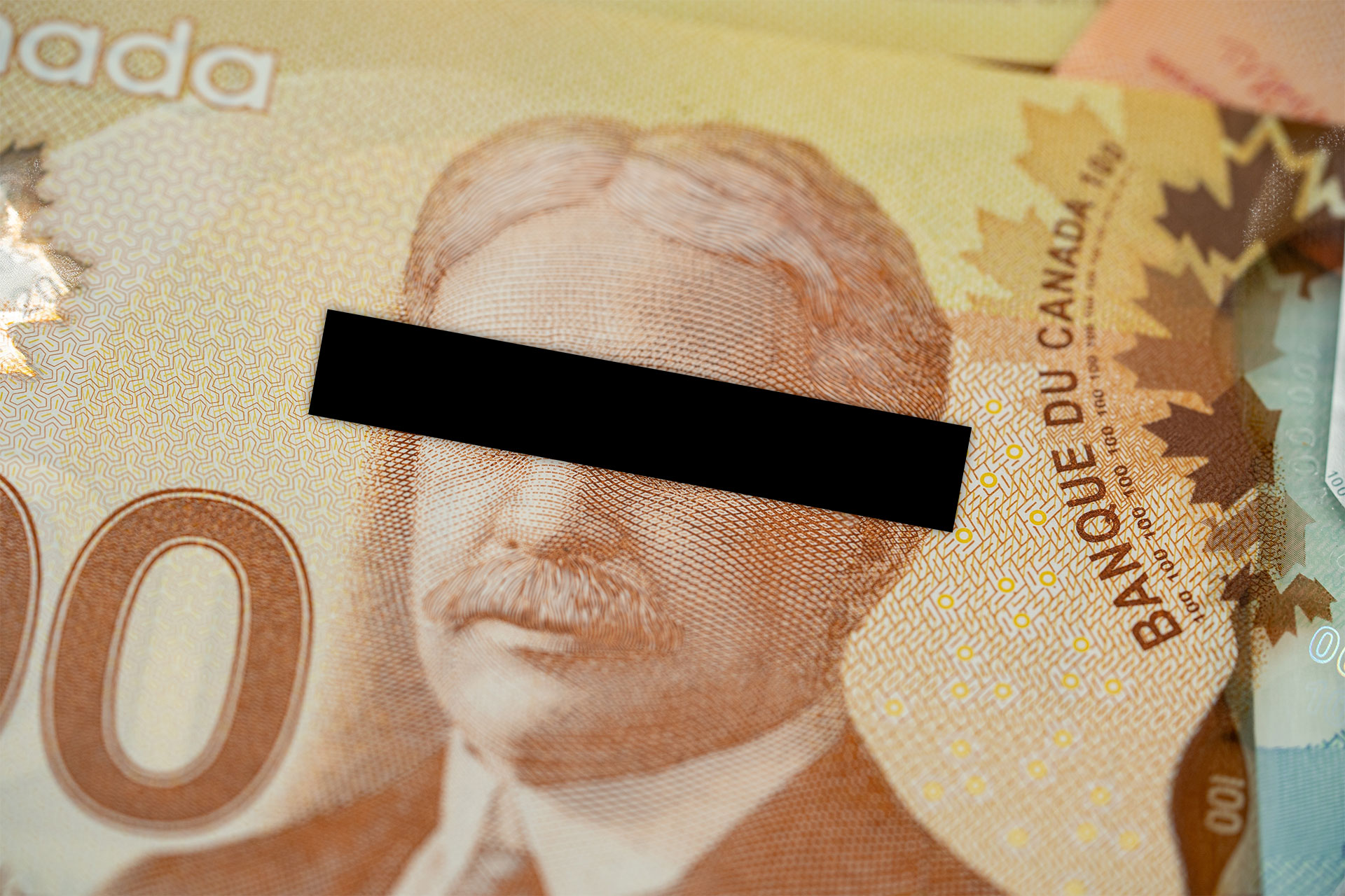Close up of Canadian one hundred dollar banknote with black bar across Sir Robert Borden's eyes